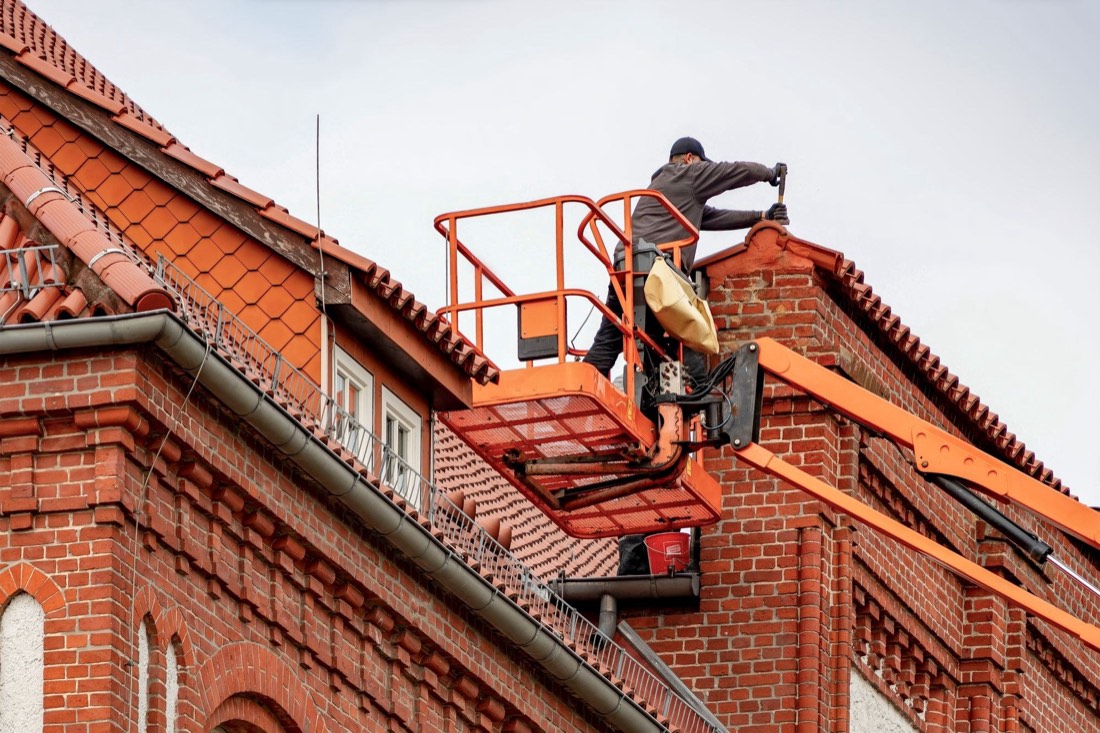 Dekarz naprawiający stary dach ceramiczny i komin z podnośnika